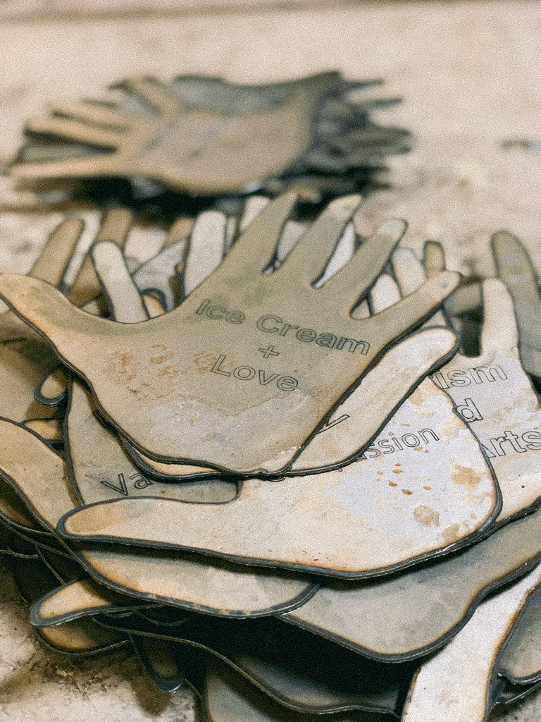 A stack of steel laser-cut hands with different inscriptions on them. The top one says "Ice cream and love."